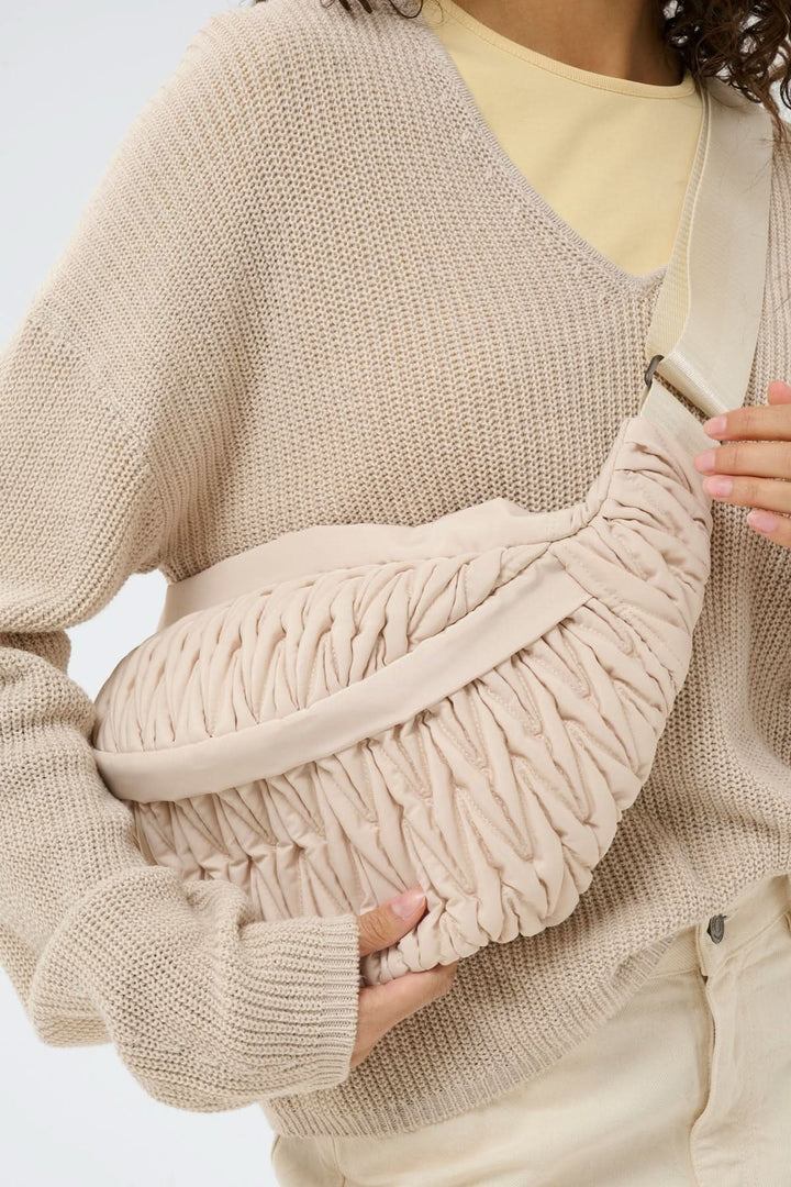 Femme portant un sac bandoulière matelassé Samy Bumbag beige avec texture froncée, ajustable et ergonomique, tenue décontractée.