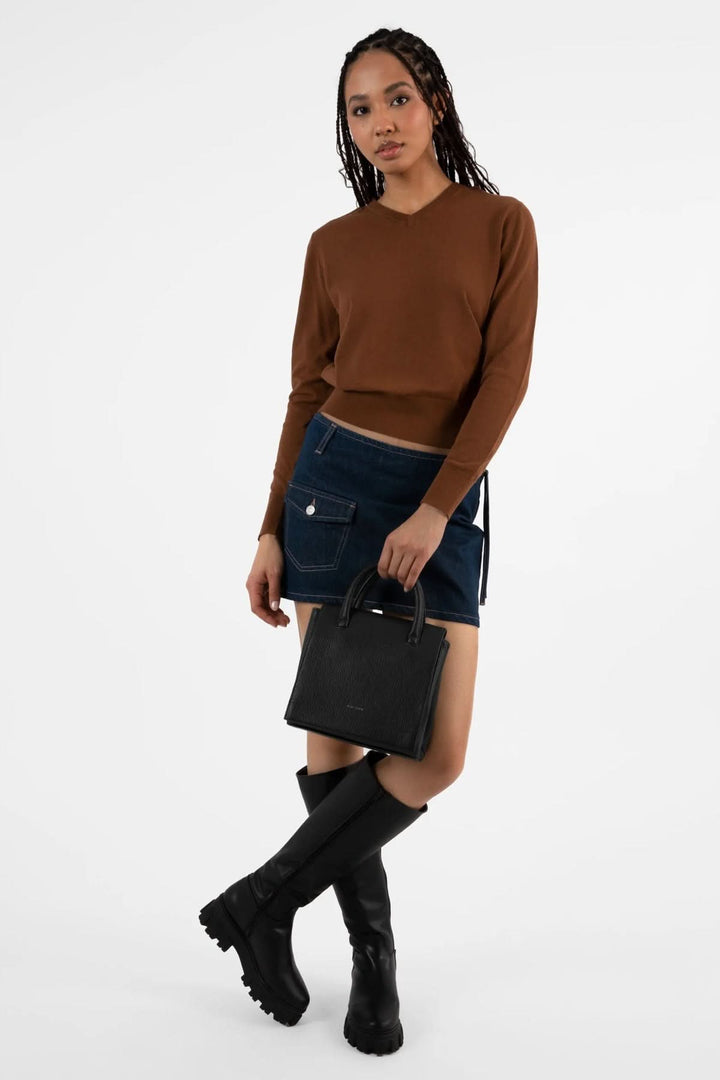 Femme portant un sac à main Adelsm avec un pull brun et une jupe en jeans, accessoirisée par des bottes noires.
