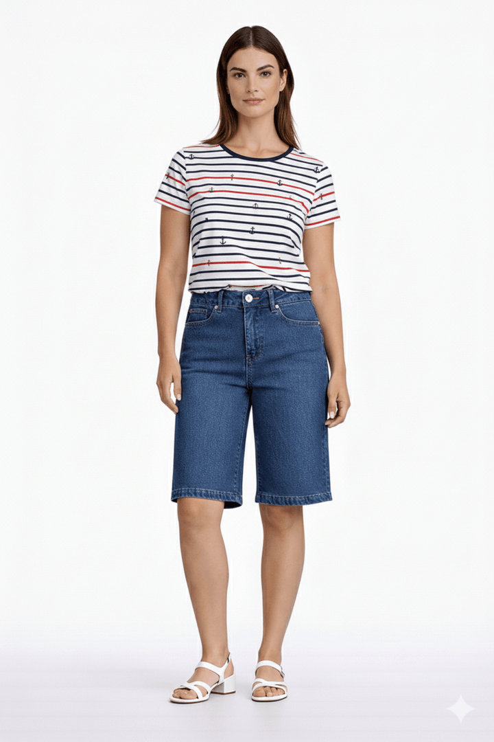 Femme portant un short bermuda ample en denim, coupe ample, longueur au genou, avec un t-shirt rayé et des sandales blanches.