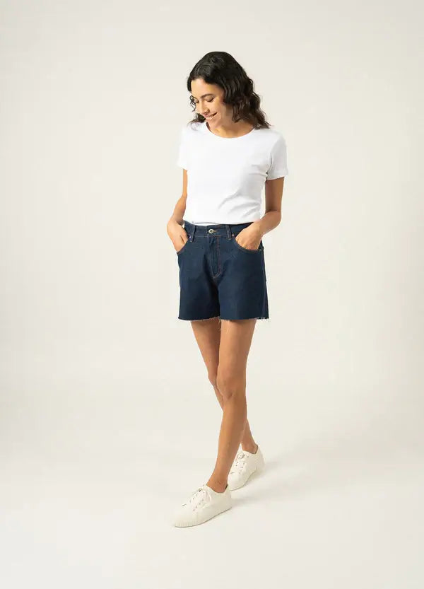 Femme portant le T-shirt AJACCIO II blanc, manches courtes, avec shorts bleu marine, style décontracté.
