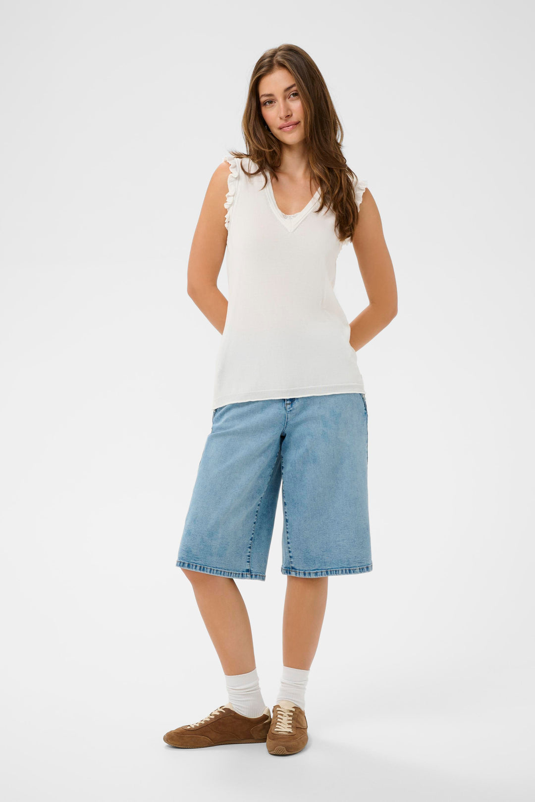 Femme portant un T-shirt Desten blanc sans manches avec décolleté en V et finitions volantées, associé à un short en jean.