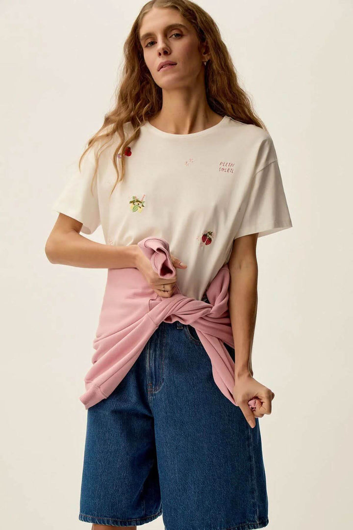 Femme portant un t-shirt Gamos avec motifs floraux, jeans en denim et un gilet rose noué autour de la taille.