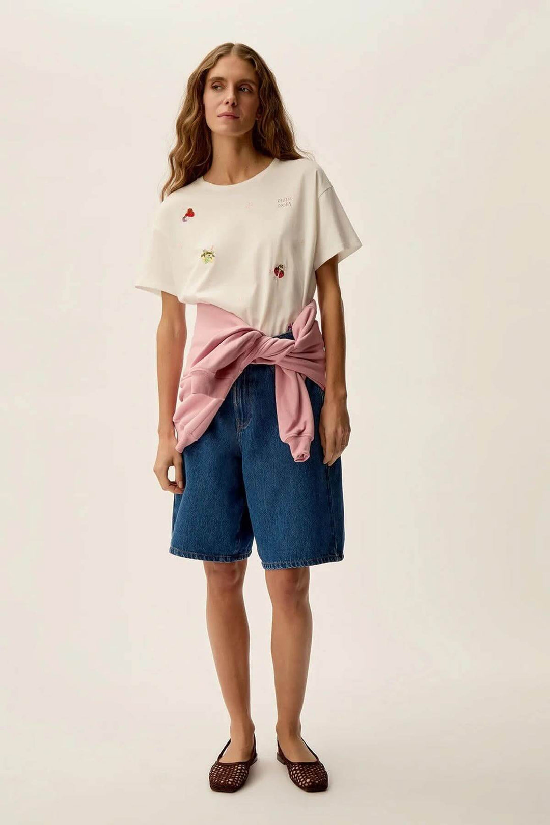 Femme portant un t-shirt Gamos avec motifs floraux et fruités, jean court, et un pull noué sur la taille.