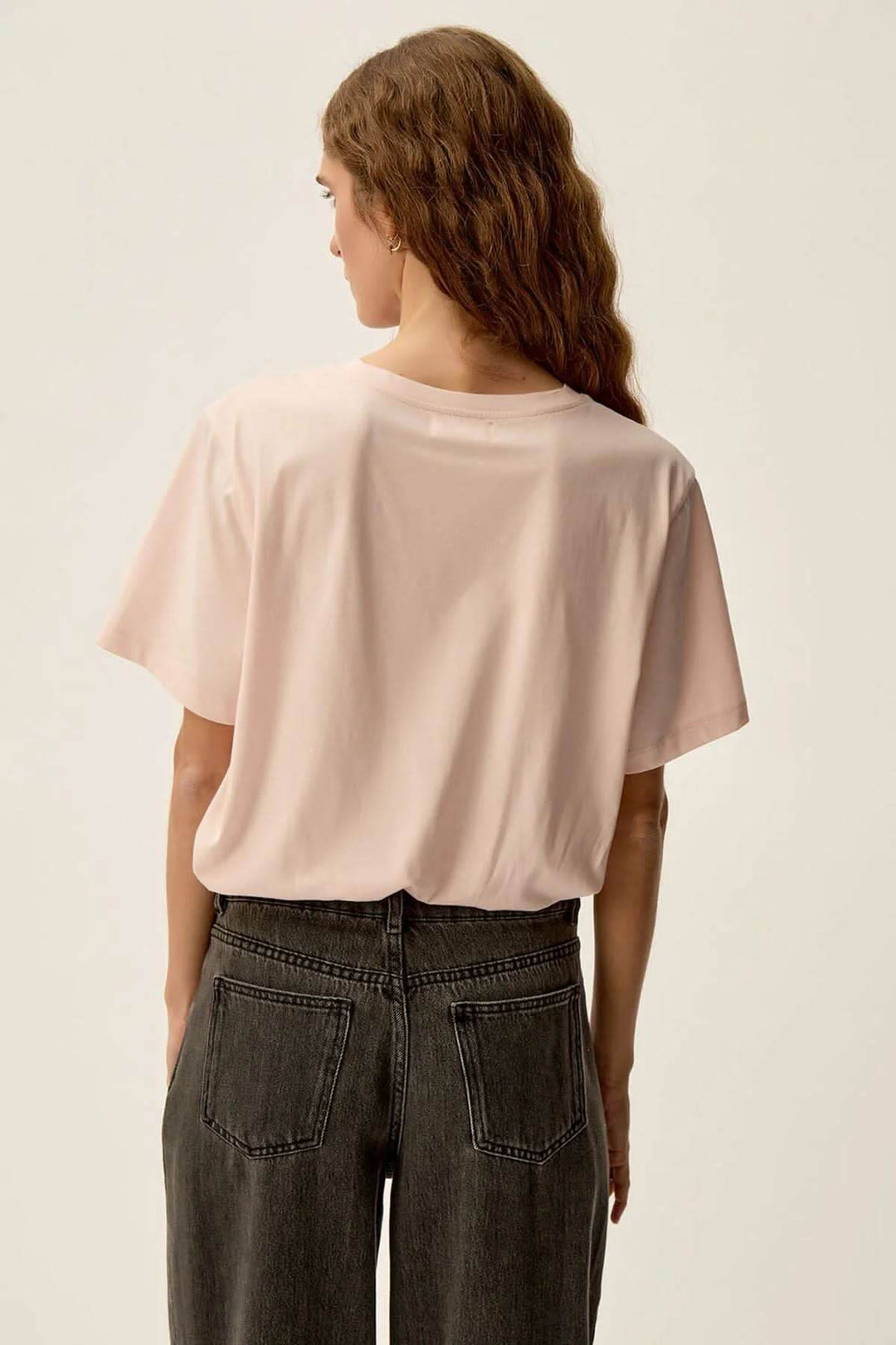 Femme vue de dos portant un t-shirt rose poudré, style minimaliste, manches courtes et coupe droite.