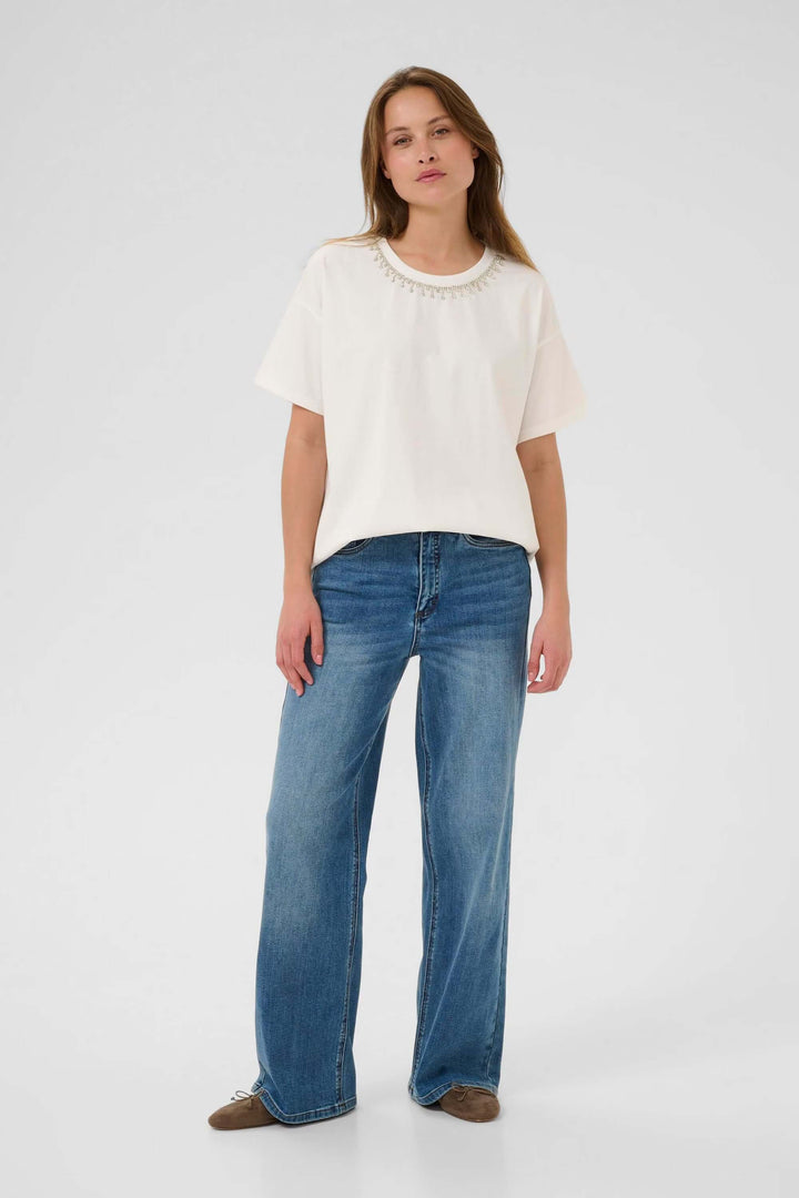 Femme portant le T-shirt Helen blanc basique à manches courtes et col rond, associé à un jean pour un look minimaliste.