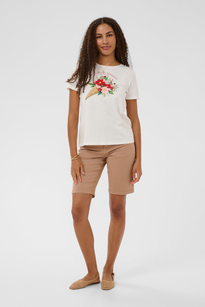 Femme portant un T-shirt Joliy blanc avec imprimé artistique, associé à un short beige pour un look décontracté et féminin.