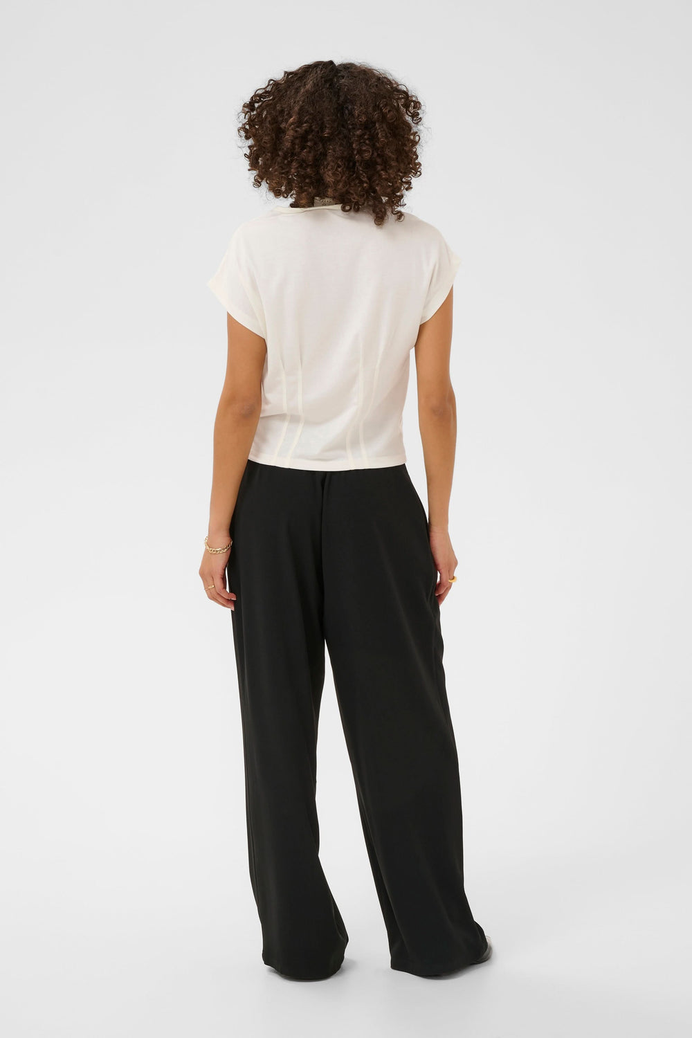 Vue de dos d'un modèle portant un T-shirt Lise fluide à manches courtes avec détails structurés, associé à un pantalon noir.