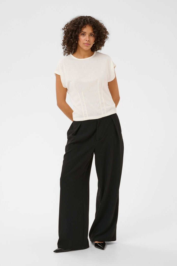 T-shirt Lise fluide à manches courtes avec détails structurés, porté avec pantalon noir, style moderne et élégant.