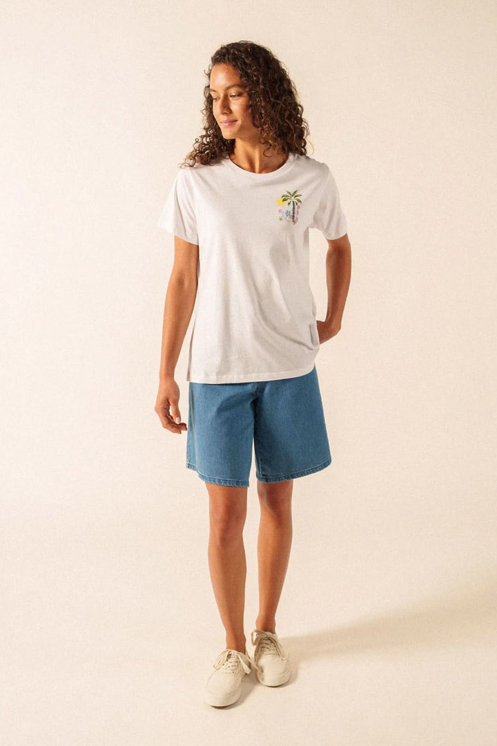 Femme portant le T-shirt Léonore blanc avec motif discret, assorti à un short en jean décontracté pour un look quotidien.