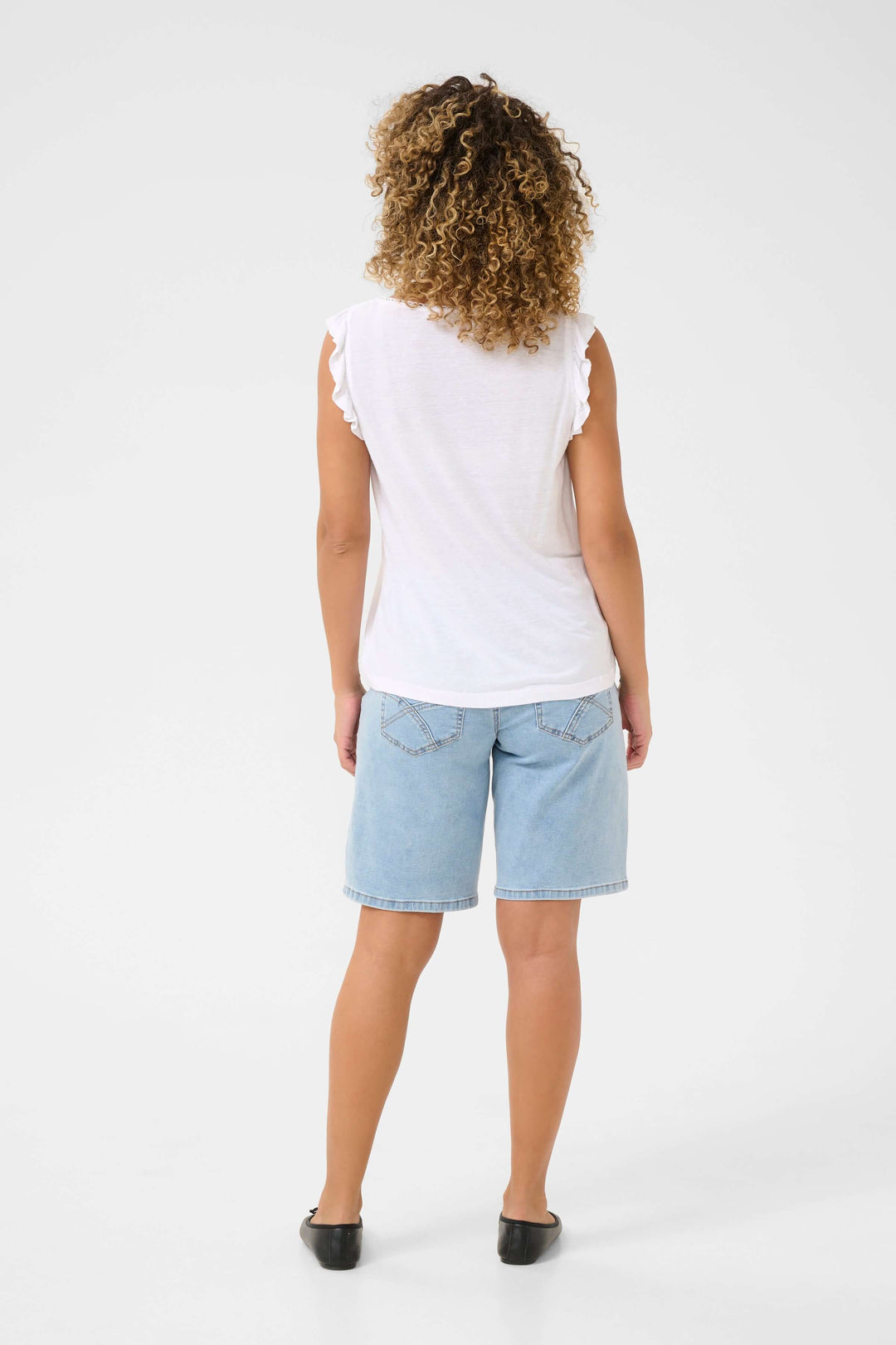 Femme portant un t-shirt sans manches blanc avec volants, vue de dos, associé à un short en jean.