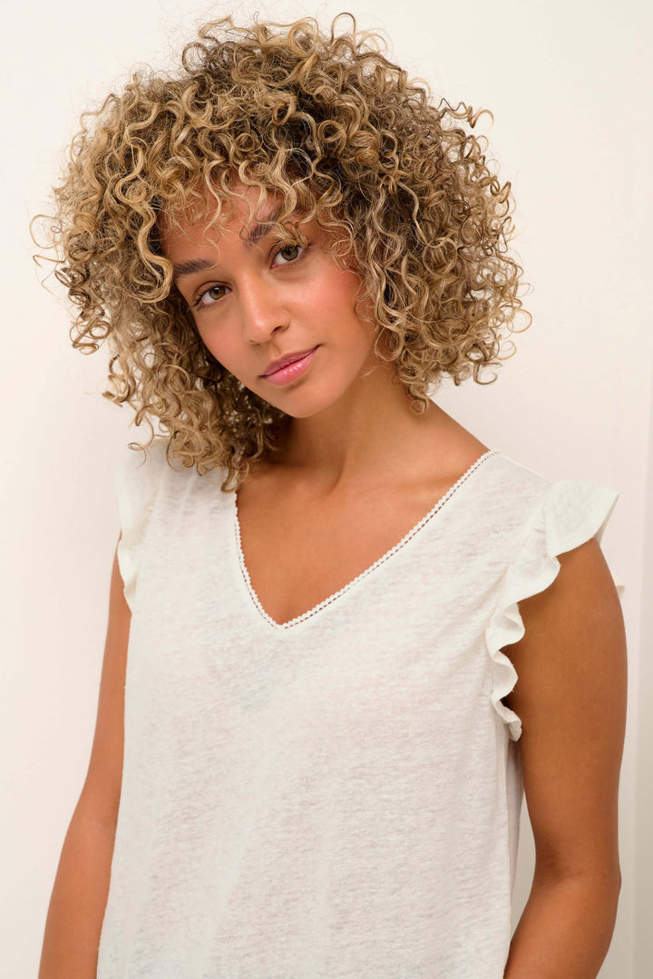 T-shirt sans manches en V, orné de dentelle et volants, porté par une femme aux cheveux bouclés.