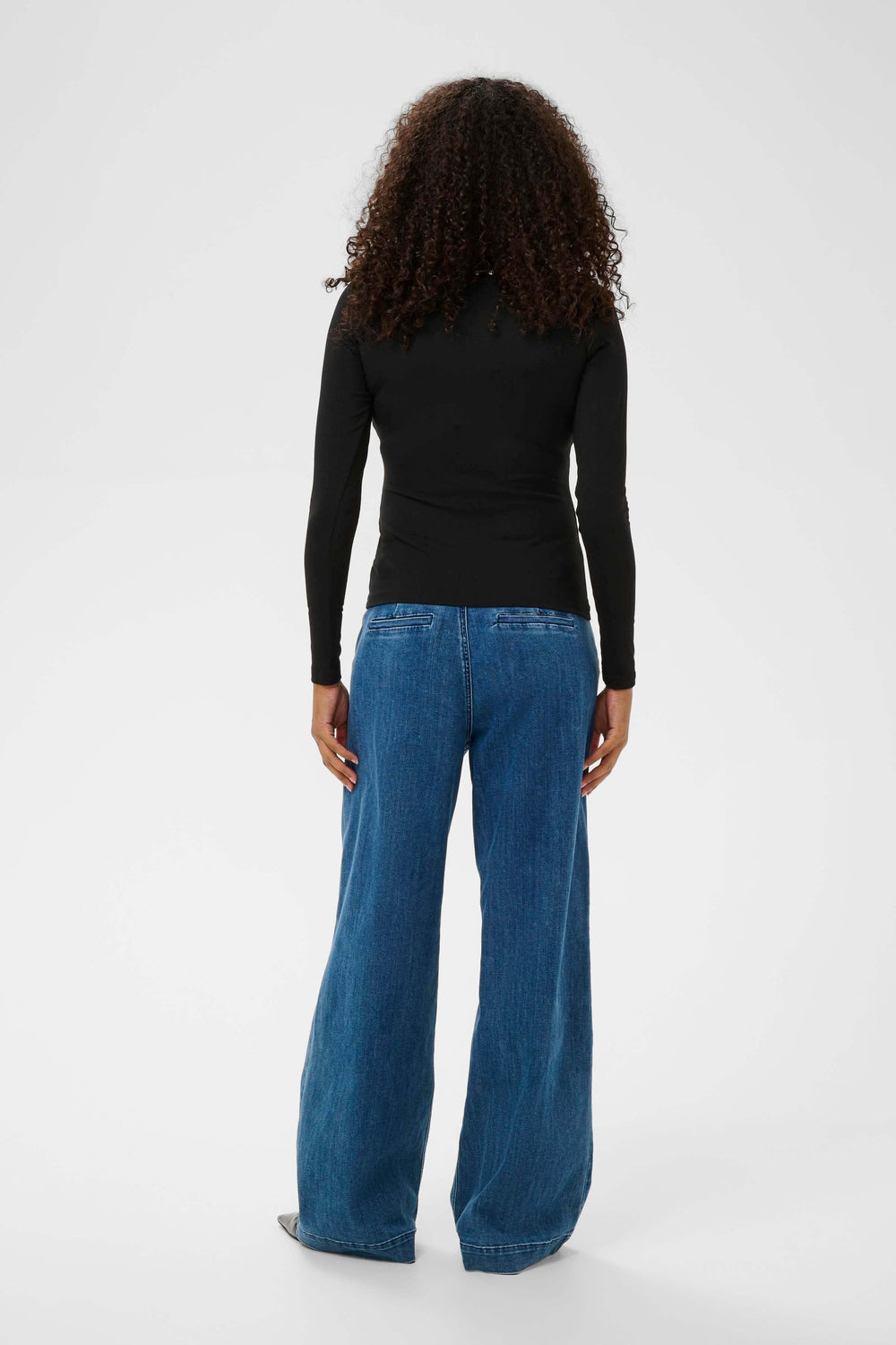 Vue arrière d'une femme portant un T-shirt Marty noir à manches longues, coupe ajustée, avec des détails décoratifs, associé à un jean large.