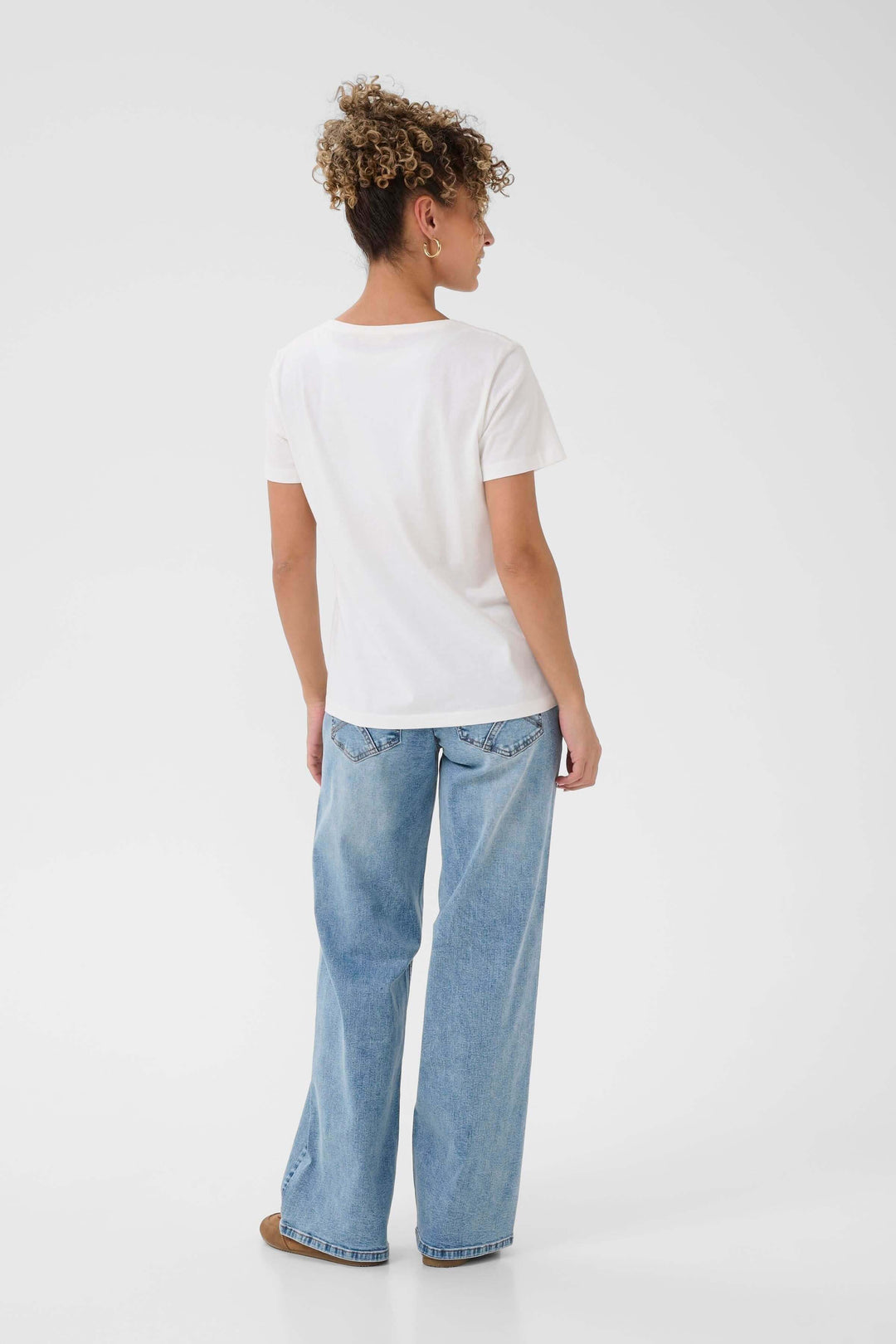 Vue arrière du T-shirt Nikita blanc avec coupe droite, encolure ronde et manches courtes, porté par une femme, jeans et chaussures marron.