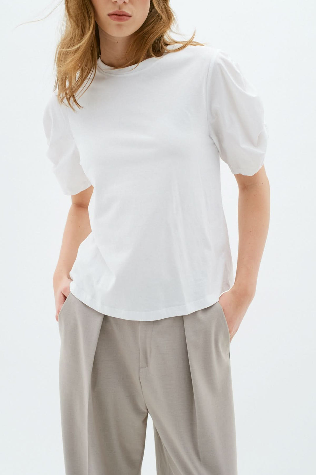 T-shirt Payana blanc classique en coton, avec manches froncées et col rond, porté avec un pantalon élégant.