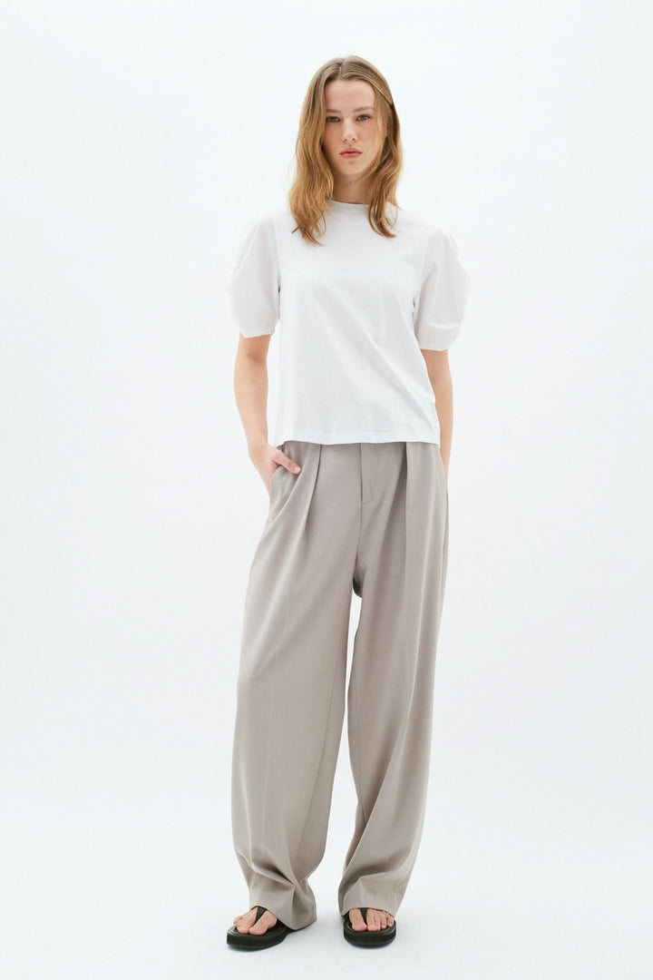 Femme portant un t-shirt Payana blanc avec manches audacieuses et pantalon beige décontracté.