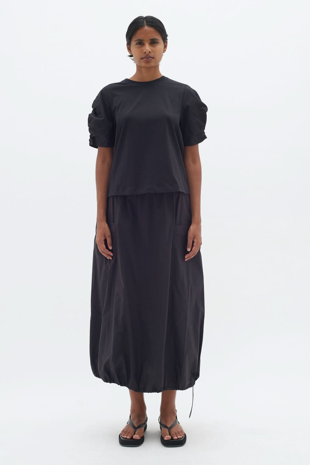 T-shirt Payana noir moderne avec manches froncées, porté avec une jupe longue, look élégant et contemporain.