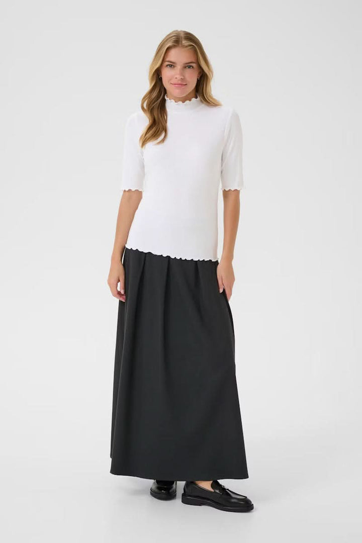 Femme portant un T-shirt Ribba à col montant côtelé blanc avec finitions festonnées, manches mi-longues, et jupe noire.