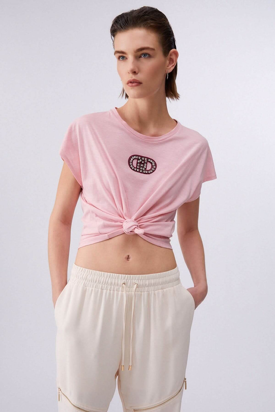 Femme portant un T-shirt avec logo décoratif, coupe décontractée, manches courtes et encolure ronde, associé à un pantalon léger.