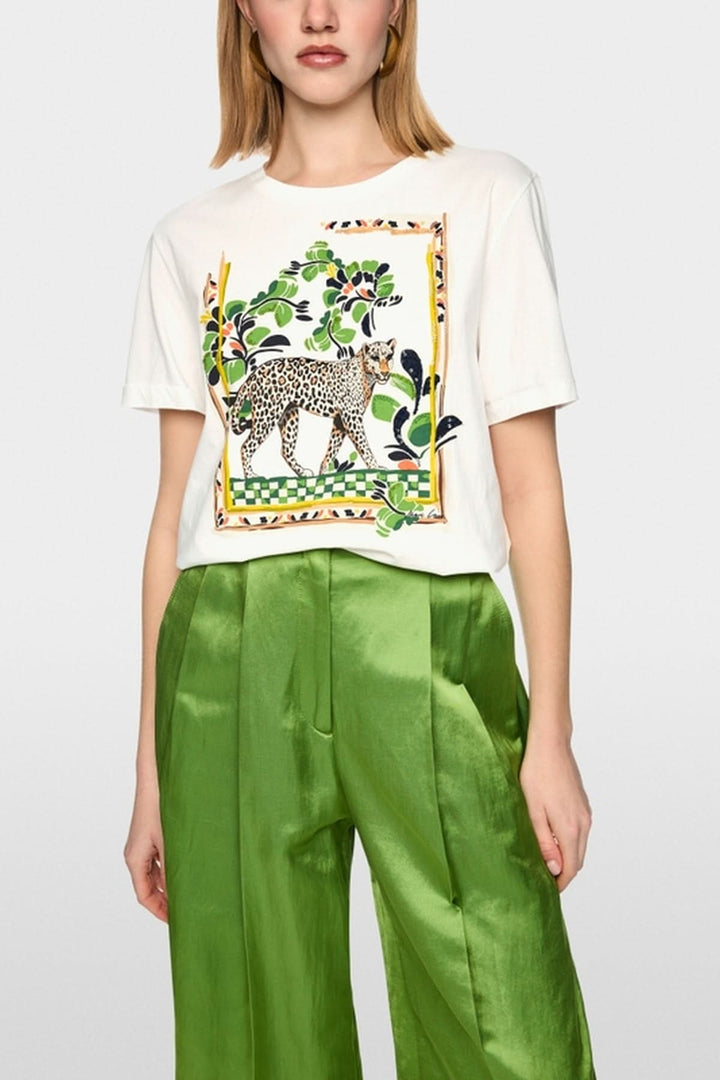 Femme portant un T-shirt avec motif léopard, manches courtes et col rond, combiné avec un pantalon vert, style ample et décontracté.