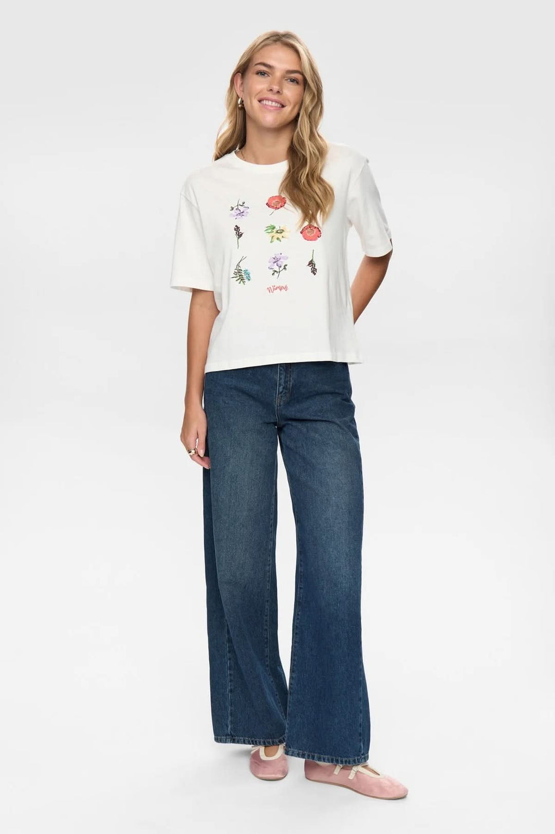 Femme portant un T-shirt à broderies florales, coupe légèrement ample, col rond classique et tissu doux, avec manches courtes.