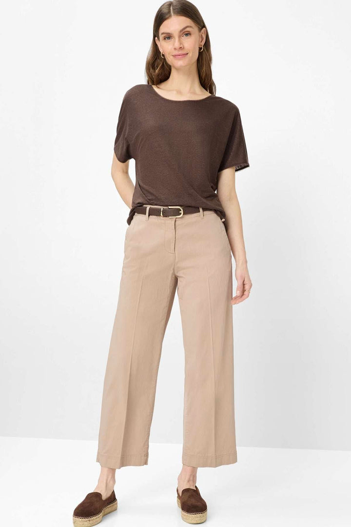 Femme portant un T-shirt col bateau Caelen marron fluide avec un pantalon beige, illustrant un style moderne et décontracté.