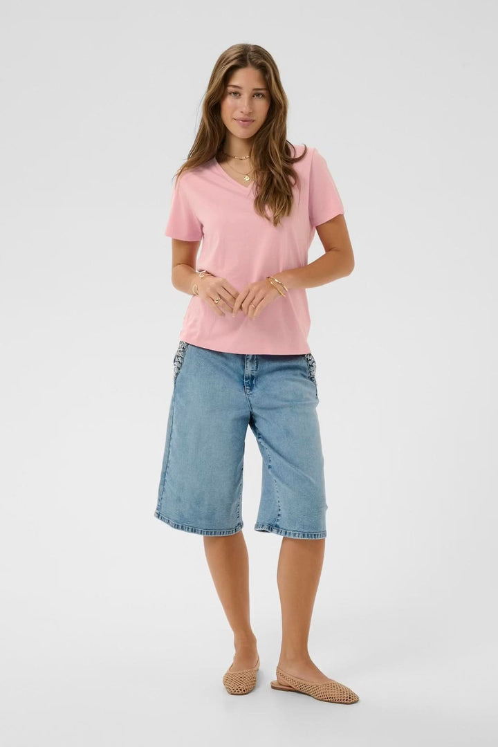 Femme portant un T-shirt col en V rose avec un short en jean, posant debout.