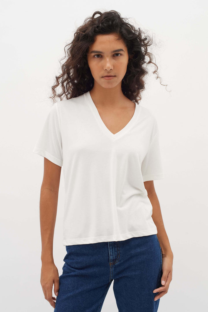 Femme portant un T-shirt col en V Liliana blanc, coupe droite et manches courtes, style moderne et confortable.