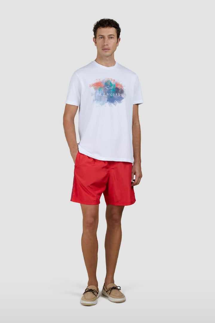 T-shirt en coton blanc avec imprimé aquarelle multicolore, porté avec un short rouge.