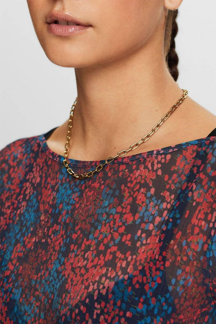 Haut en mesh plissé à motifs colorés, avec décolleté dégagé et collier en chaîne doré.