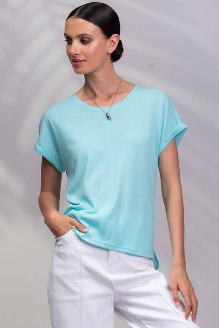 T-shirt encolure ronde en bleu clair, manches courtes, porté avec un pantalon blanc.