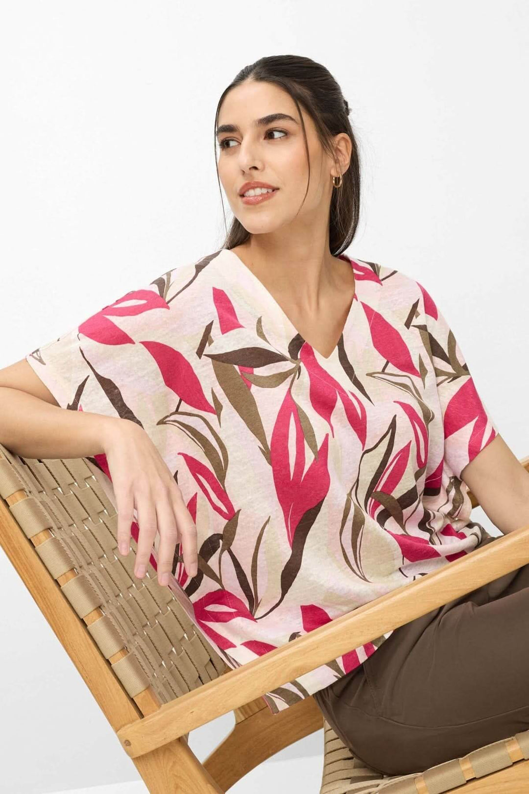 Femme portant le T-shirt imprimé végétal Cassie avec encolure en V et coupe ample dans une chaise en bois, style quotidien décontracté.