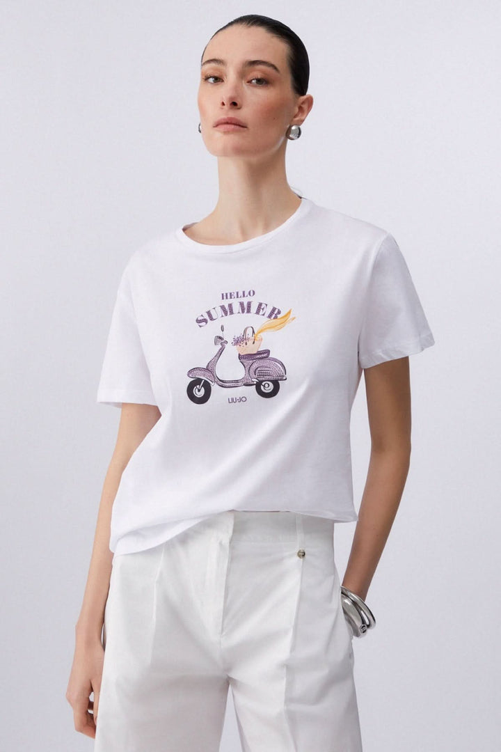 Femme portant un T-shirt à manches courtes avec imprimé graphique et pantalon blanc, look décontracté et moderne.