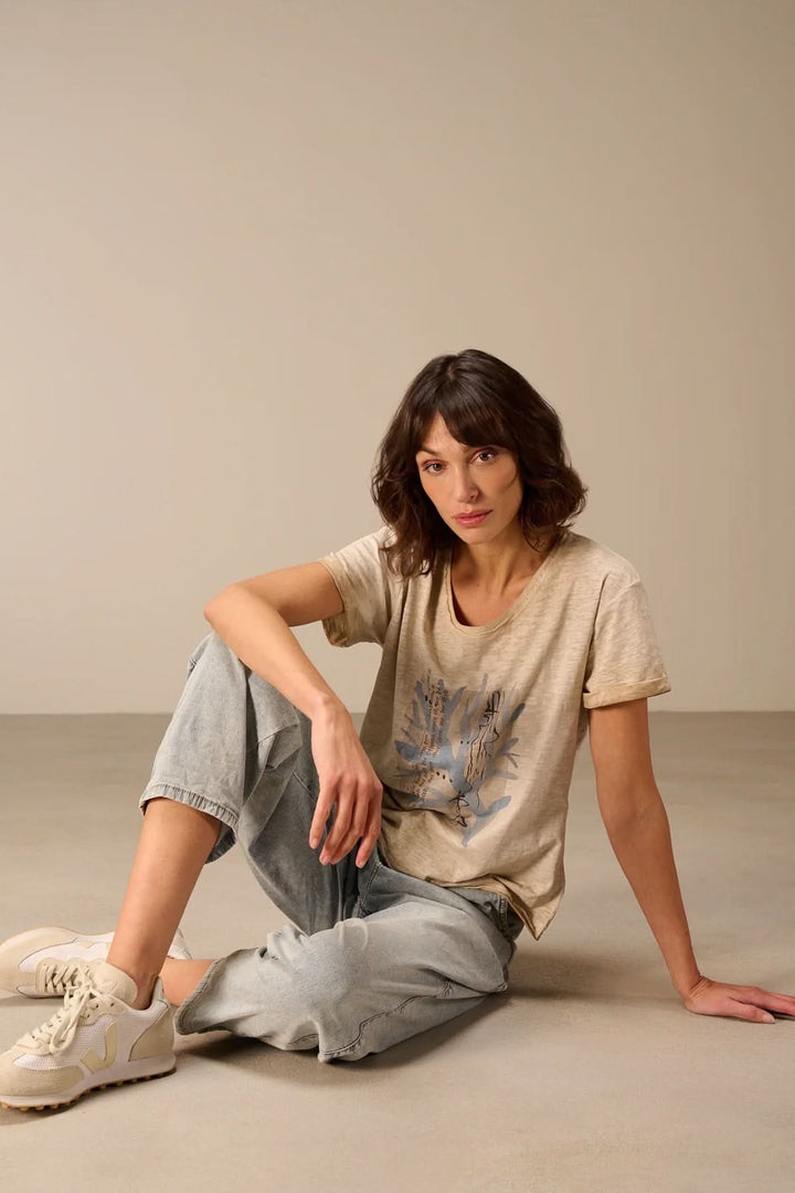 Femme portant un T-shirt à manches courtes coupe décontractée beige assise sur le sol, style mode et confort décontracté.