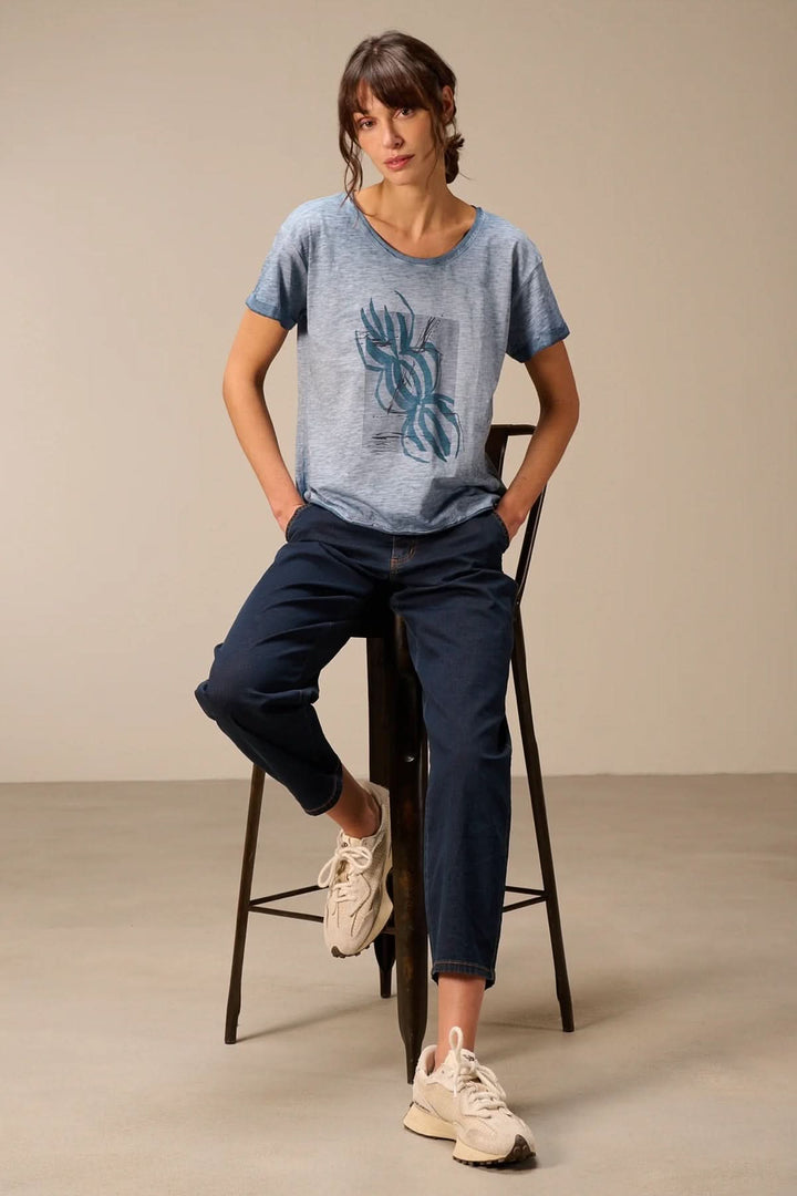 Femme portant un t-shirt à manches courtes coupe décontractée assise sur un tabouret, mettant en valeur un style décontracté moderne.