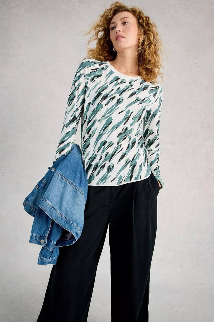 Femme portant le T-shirt à manches longues Clara avec motif abstrait, tenant une veste en jean drapée sur l'épaule.