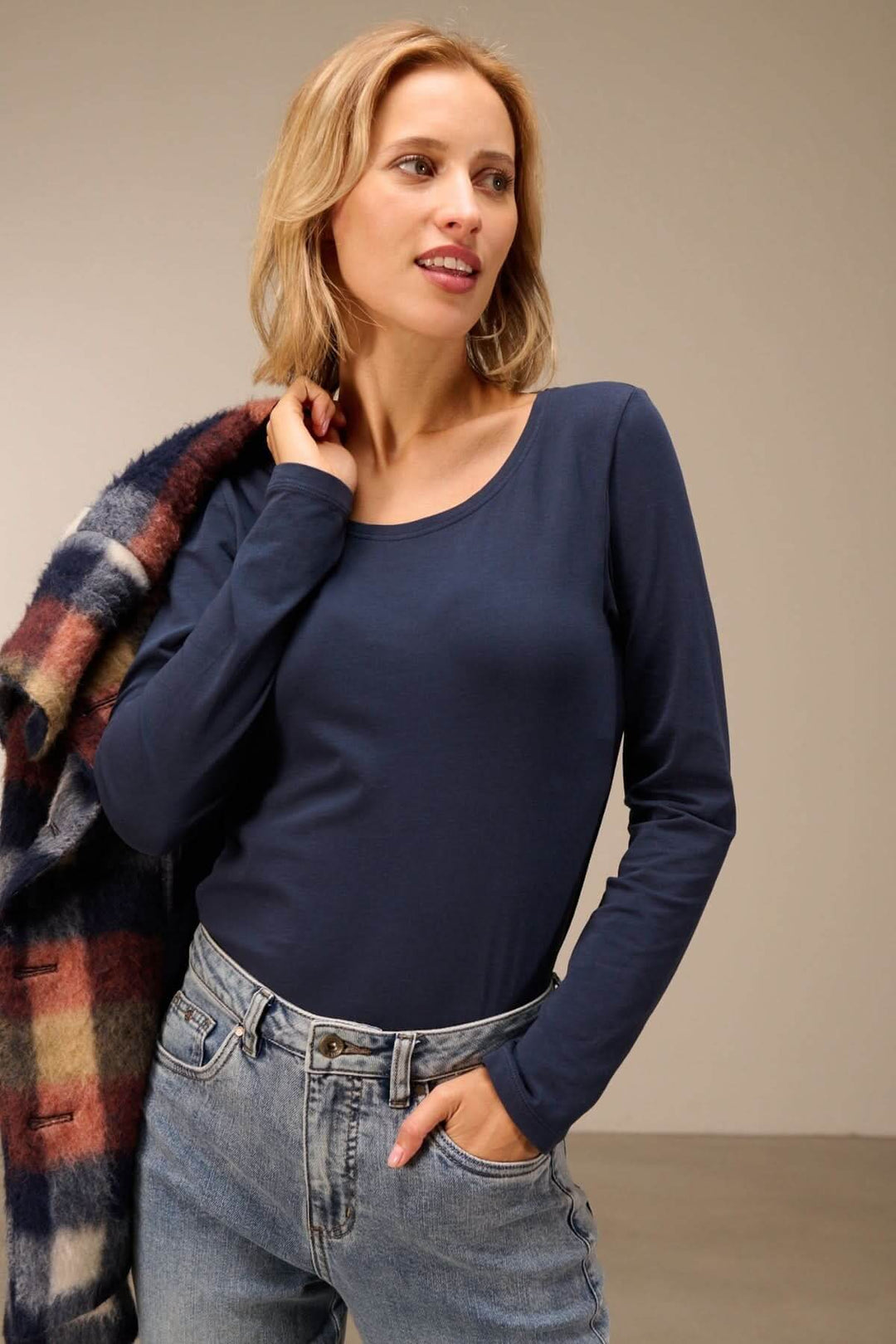 Modèle portant un T-shirt manches longues col rond — jersey doux extensible, entrée dans un jean, avec un manteau à carreaux sur l&