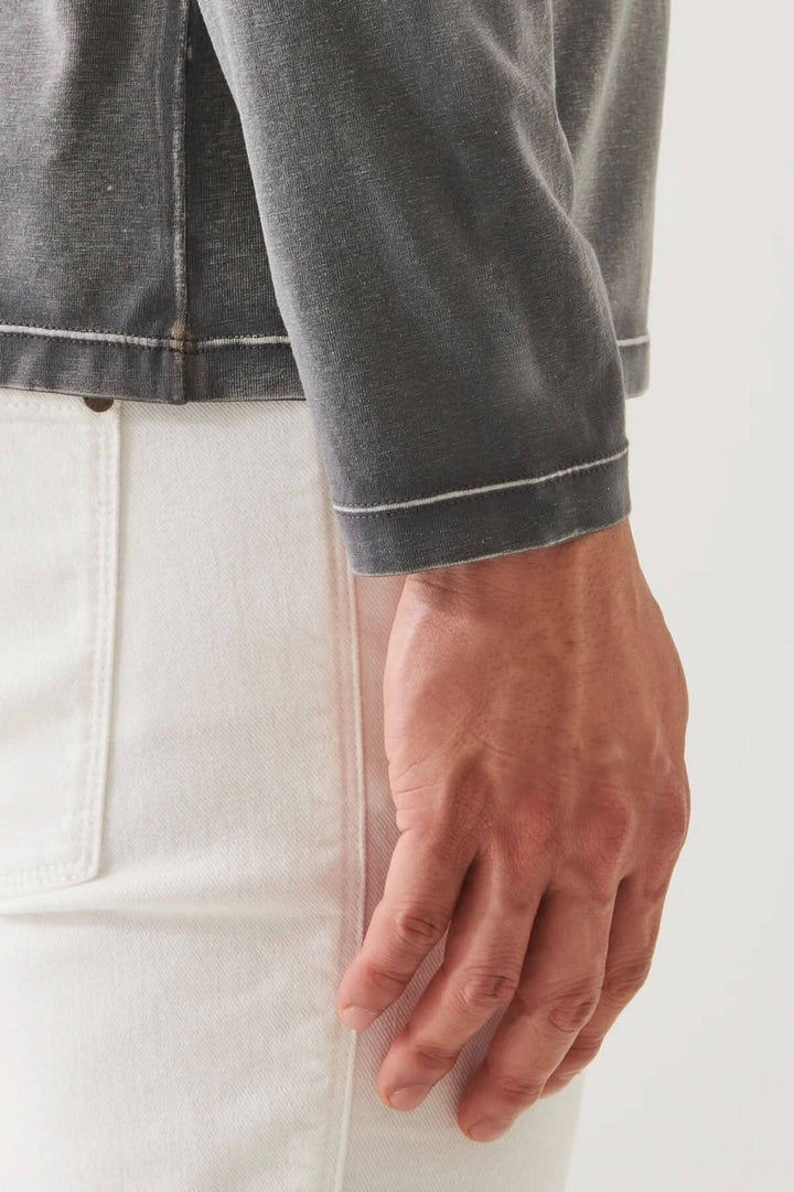 Détail du t-shirt à manches longues en coton pima avec couture vintage et main sur le pantalon blanc.