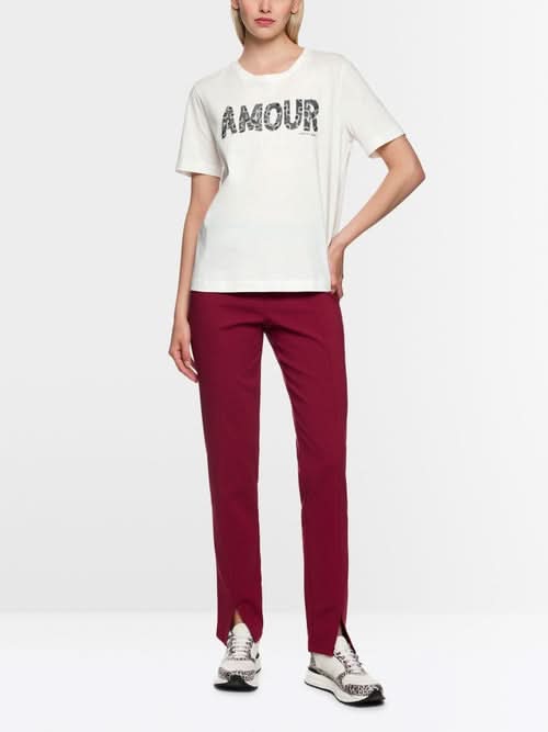 T-shirt à paillettes blanc avec slogan "Amour", col rond, manches courtes, porté par mannequin en pantalon rouge.