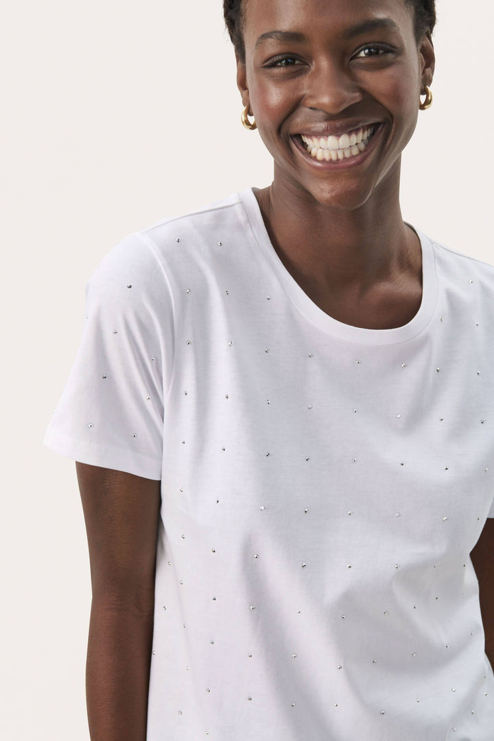 Femme souriante portant un t-shirt scintillant en coton biologique, design simple avec détails en strass.
