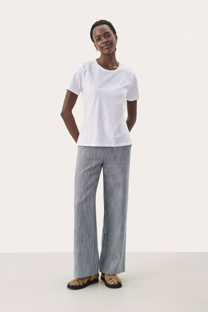 Femme portant un t-shirt blanc simple et un pantalon rayé, style décontracté et élégant.