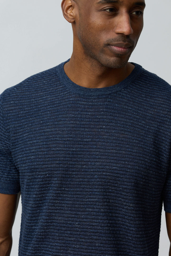 Homme portant un T-shirt texturé en lin et soie, coupe ajustée, col rond et manches courtes, couleur bleue.