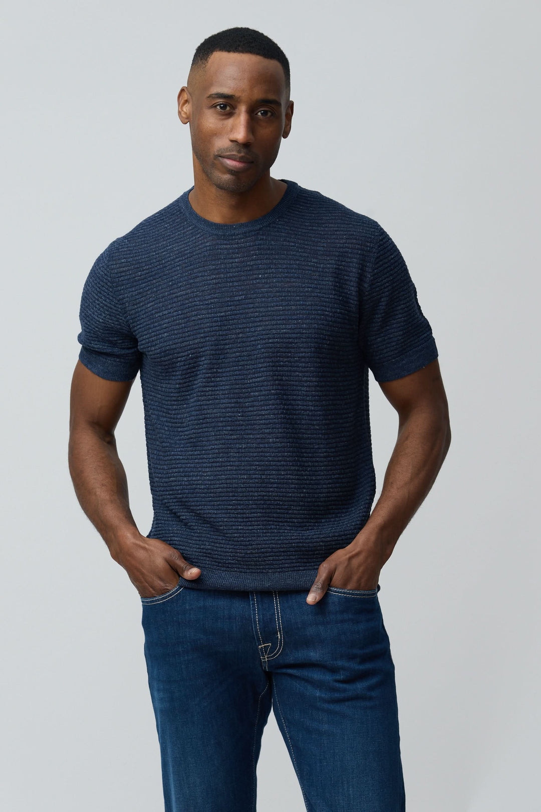 Homme portant un T-shirt texturé en lin et soie, coupe ajustée, manches courtes, maille texturée, tenue moderne et épurée.