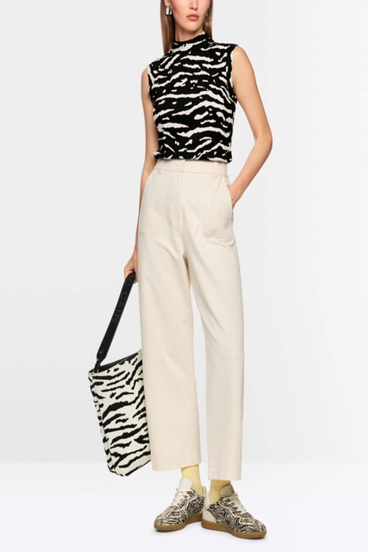 Top avec imprimé animalier sans manches, col montant, porté avec un pantalon blanc, sac et chaussures assortis en fond neutre.