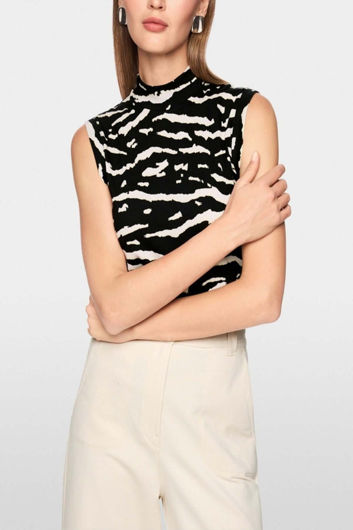 Top avec imprimé animalier sans manches, col montant, maille côtelée, porté par femme, fond blanc.