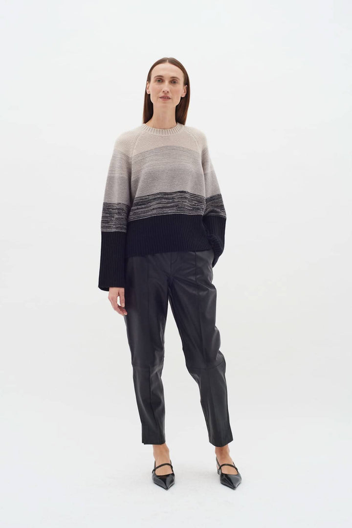 Modèle portant un pull tricot côtelé aux larges rayures neutres, associé à un pantalon en cuir noir.