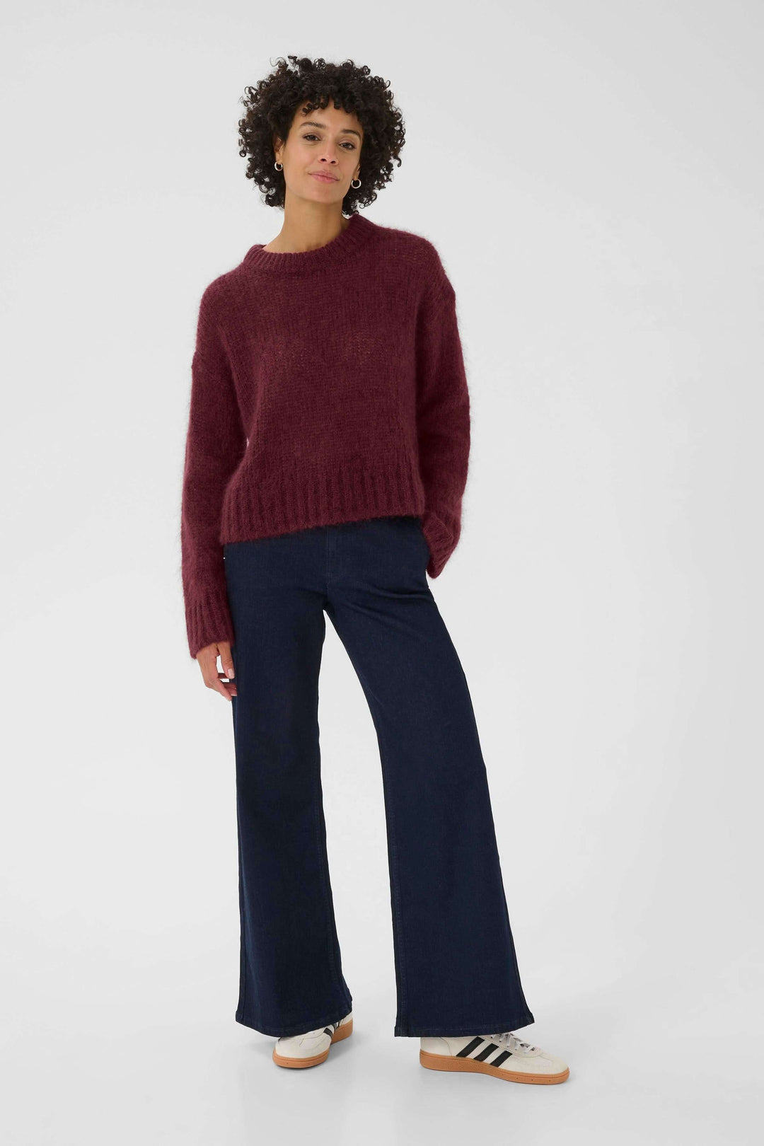 Femme portant un tricot ample bordeaux à col rond avec un pantalon élégant, parfait pour la saison froide.