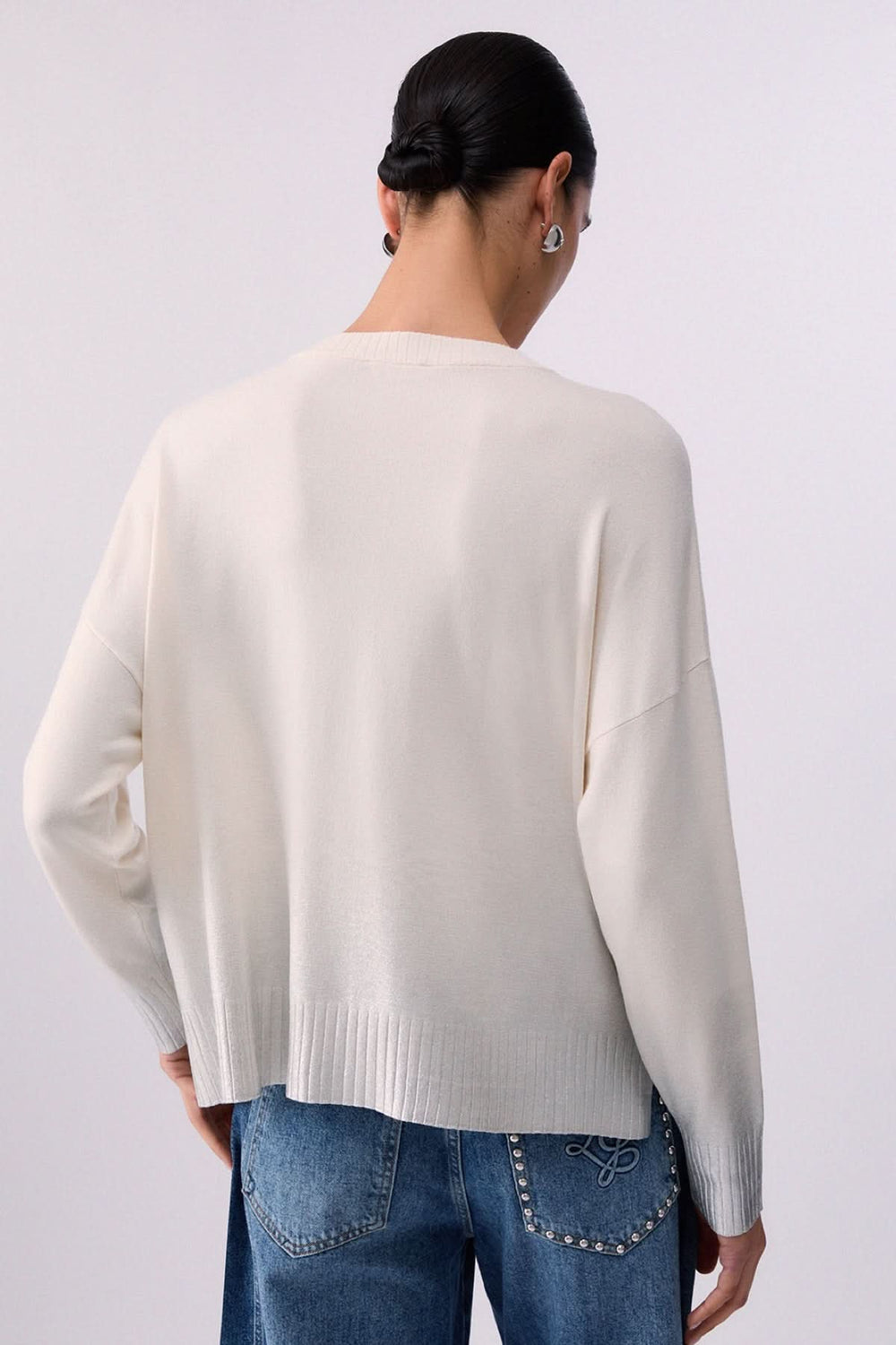 Vue arrière d'un tricot blanc à col en V à manches trois-quarts, porté avec un jean, soulignant la coupe fluide et les poignets côtelés.