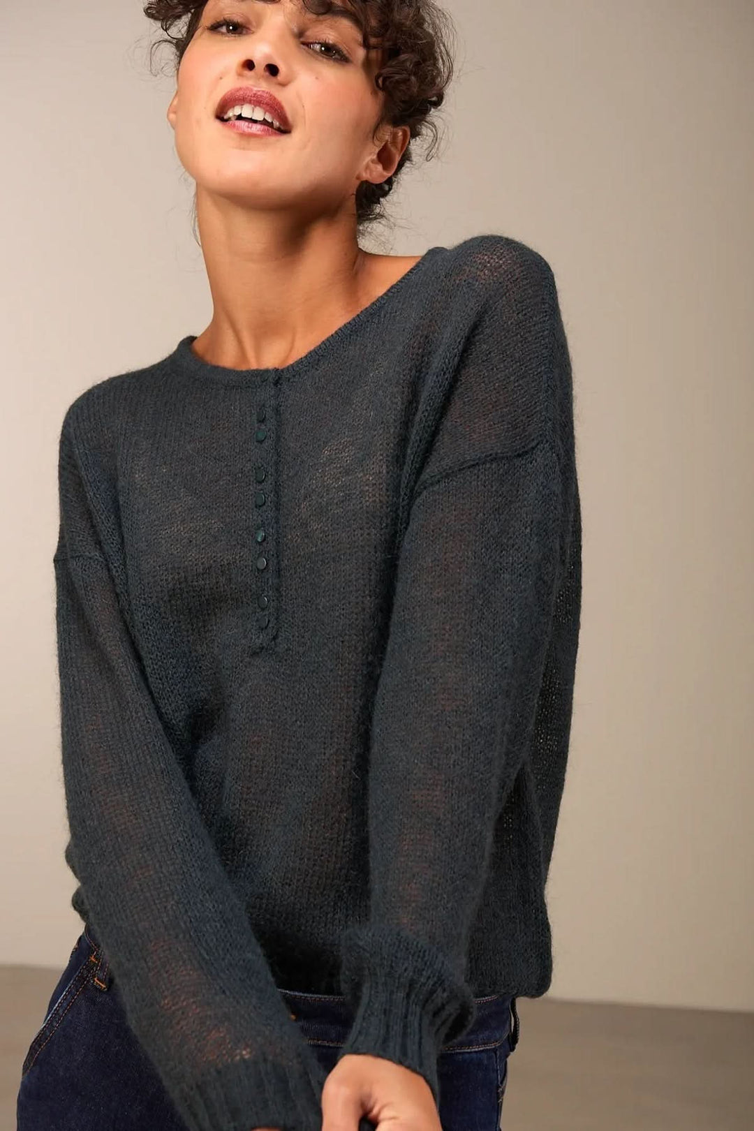 Femme portant un tricot doux en maille légère, légèrement transparent, avec patte de boutonnage et coupe décontractée.