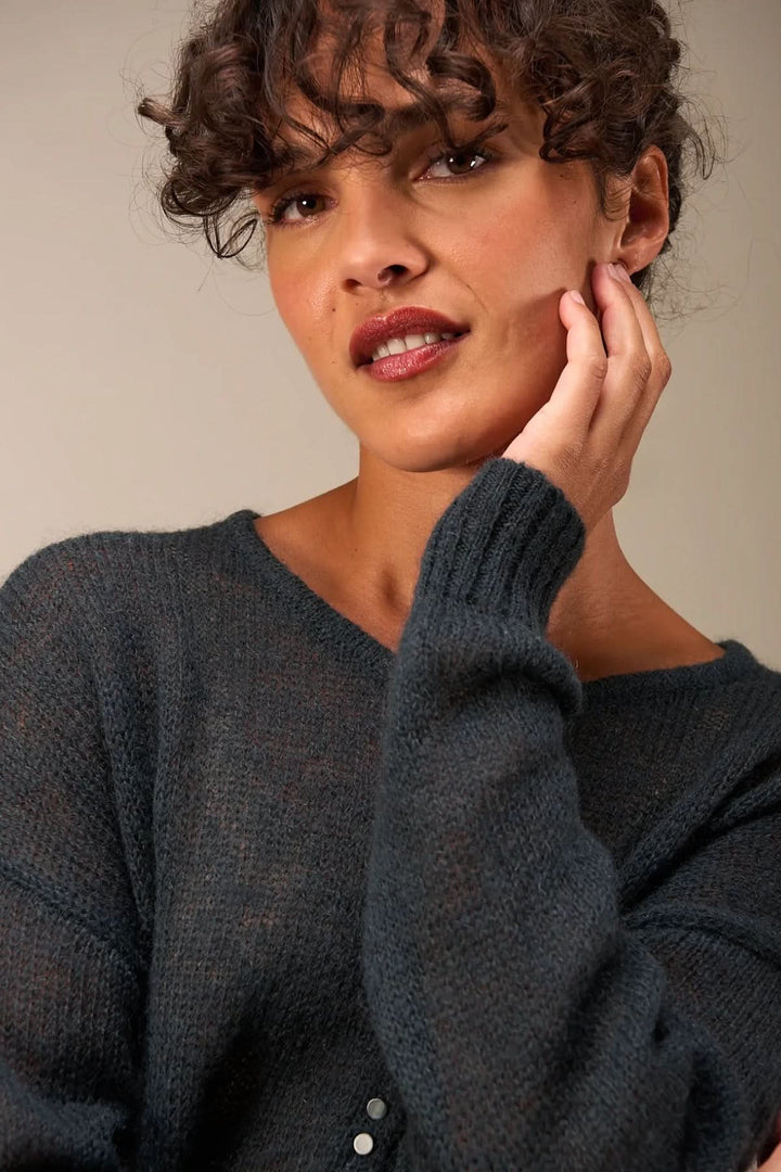 Femme portant un tricot doux, légèrement transparent, avec patte de boutonnage, idéal pour superposer et créer un style décontracté.