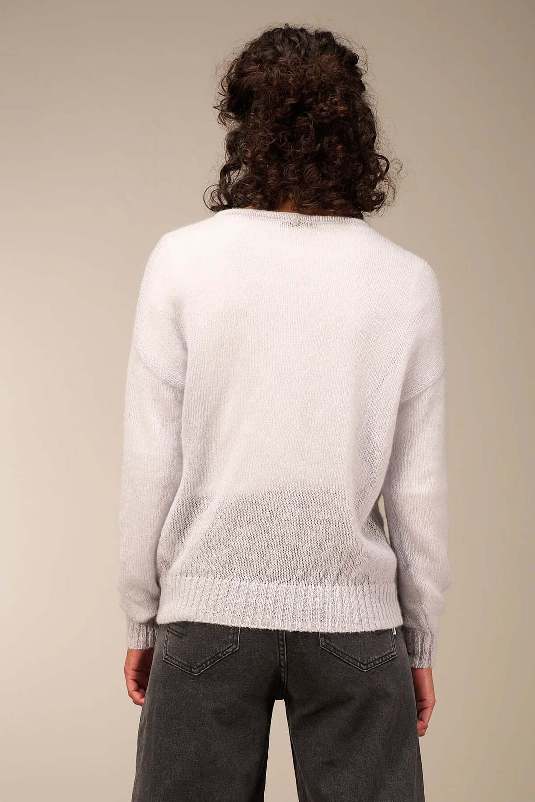 Person wearing a light, airy knit sweater in white with decorative buttons, paired with high-waisted denim, showcasing a casual fall style.